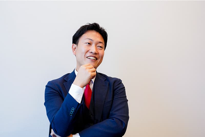 萩原駿也が自然な笑顔で話を聞いているポートレート写真